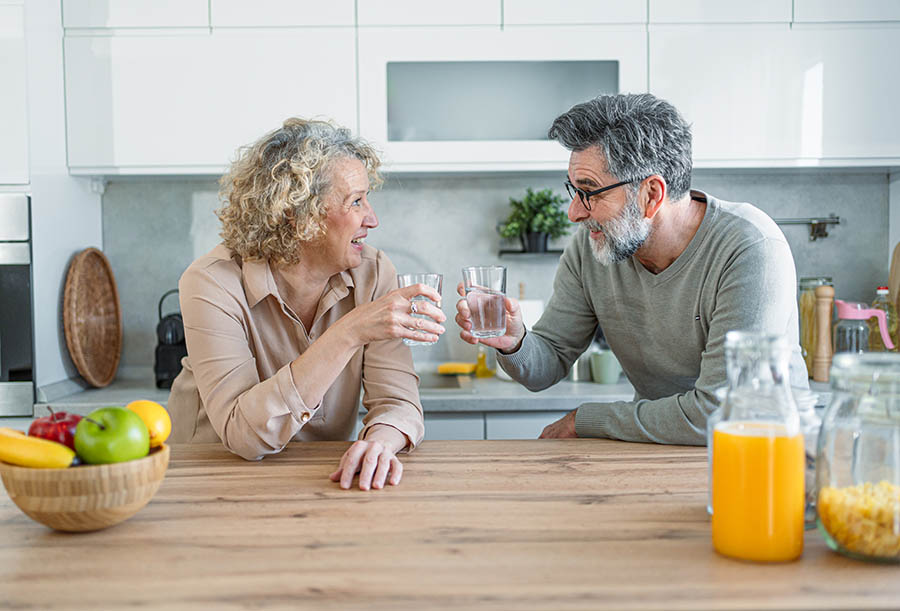 Cheerful mature couple drinking water and relaxing in the kitchen at home
